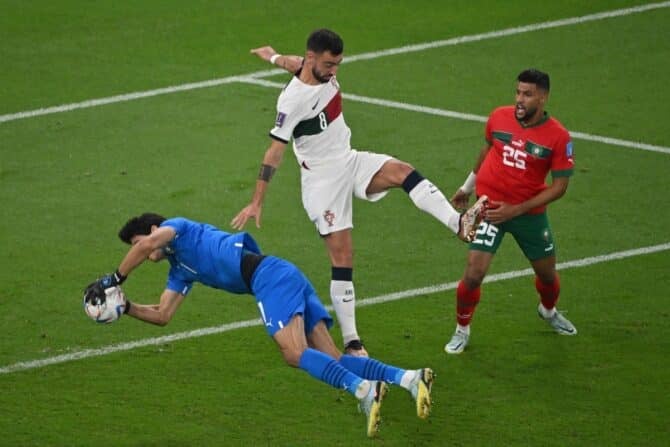 Portugals Mittelfeldspieler (Nr. 08) Bruno Fernandes attackiert Marokkos Torhüter (Nr. 01) Yassine Bounou, während Marokkos Verteidiger (Nr. 25) Yahya Attiyallah während des Viertelfinales der Fußballweltmeisterschaft Katar 2022 zwischen Marokko und Portugal im Al-Thumama-Stadion in Doha am 10. Dezember 2022 zusieht. (Foto: NELSON ALMEIDA / AFP)