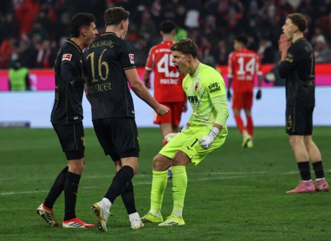 Der deutsche Torwart #01 Finn Dahmen von Augsburg feiert mit dem Schweizer Verteidiger #16 Cedric Zesiger von Augsburg nach dem 1:2-Sieg im deutschen Erstligaspiel der Bundesliga zwischen dem FC Bayern München und dem FC Augsburg am 24. Januar 2026 in München. (Foto: Alexandra BEIER / AFP)