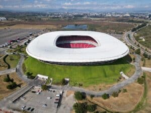 Das Estadio Akron in Guadalajara aus der Vogelperspektive – die futuristisch geformte Arena mit dem charakteristischen weißen Dach und roten Sitzreihen ist Heimstadion des Club Deportivo Guadalajara (Chivas) und einer der Spielorte der FIFA Fußball-Weltmeisterschaft 2026 in Mexiko. (Copyright Depositphotos.com)