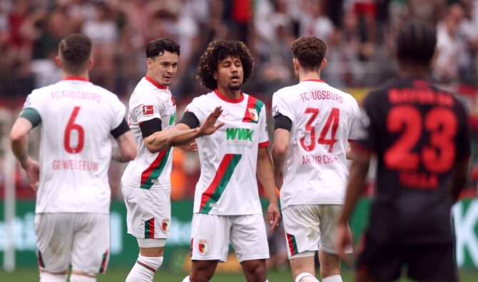 FC-Augsburg-Spieler, darunter Jan Gouweleeuw (Nr. 6) und Arthur Chaar (Nr. 34), diskutieren im Bundesliga-Auswärtsspiel bei Bayer Leverkusen 2026 – rechts im Bild läuft ein Leverkusener Spieler vorbei. (Getty Images)