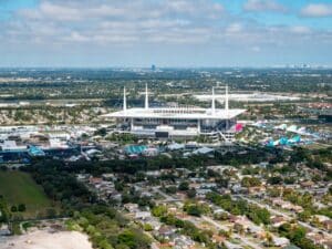 Luftaufnahme des Hard Rock Stadium in Miami Gardens, Florida – Austragungsort der FIFA Fußball-Weltmeisterschaft 2026. Die Drohnenaufnahme zeigt das Stadion mit seinem markanten weißen Zeltdach inmitten des Stadtgebiets, aufgenommen anlässlich des Super Bowl LIV. In der Ferne ist die Skyline von Miami zu erkennen. (Copyright Depositphotos.com)
