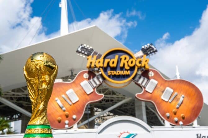 Der FIFA-WM-Pokal vor dem Eingang des Hard Rock Stadium in Miami Gardens, Florida – Austragungsort der FIFA Fußball-Weltmeisterschaft 2026. Im Hintergrund prangt das markante Logo des Hard Rock Stadium mit den gekreuzten Gitarren. Das Stadion ist Heimspielstätte der Miami Dolphins aus der NFL. (Copyright Depositphotos.com)
