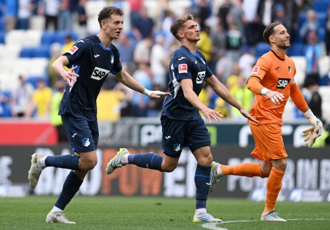 Zwei Hoffenheimer Spieler bejubeln einen Treffer gegen Borussia Dortmund in der Bundesliga-Partie 2026, während der enttäuschte BVB-Torhüter das Geschehen an sich vorüberziehen lässt. (Getty Images)