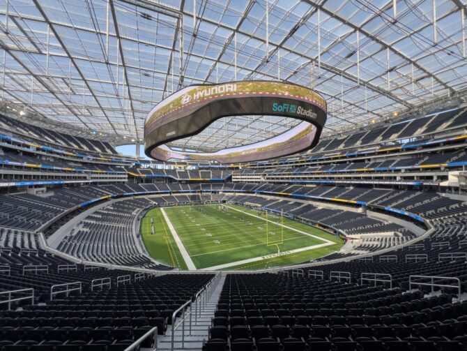 Innenansicht des SoFi Stadium in Inglewood bei Los Angeles, USA – Austragungsort der FIFA Fußball-Weltmeisterschaft 2026. Der Blick von den Rängen zeigt den gepflegten Rasen und das markante ringförmige Anzeigetafelsystem unter dem transparenten Membrandach des modernen NFL-Stadions, Heimstadion der Los Angeles Rams und der Los Angeles Chargers. (Copyright Depositphotos.com)