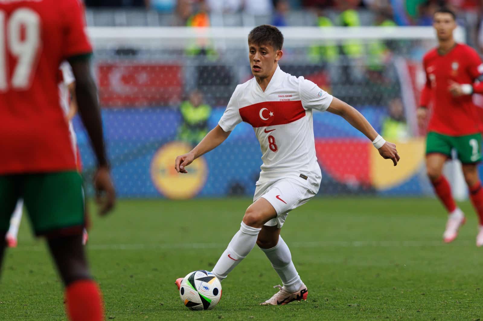 Ein türkischer Nationalspieler mit der Rückennummer 8 am Ball im weißen Nike-Trikot der türkischen Nationalmannschaft. Im Hintergrund ist Cristiano Ronaldo im roten Portugal-Dress zu erkennen. Das Bild zeigt das neue Nike-Trikot der Türkei vor der WM 2026. (Copyright Depositphotos.com)