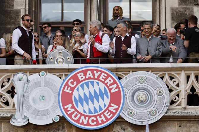 Spielerinnen und Spieler des FC Bayern feiern gemeinsam auf dem Balkon des Münchner Rathauses. Vor der Kulisse des Marienplatzes präsentierten die Doppelmeister am 18. Mai 2025 ihre Trophäen: Sowohl die Männer als auch die Frauen hatten in der Saison 2024/25 die Meisterschaft in ihrer jeweiligen Liga gewonnen. (Johannes Simon / Getty Images Europe via Getty Images)