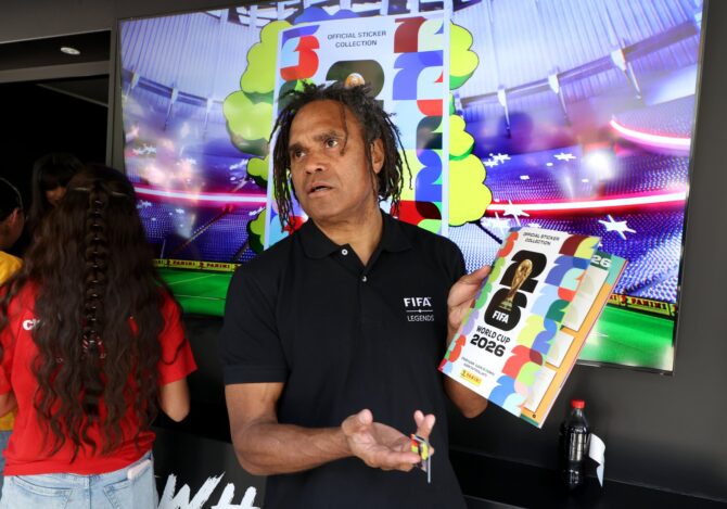 Eine FIFA-Legende präsentiert beim Community-Event der FIFA World Cup Trophy Tour by Coca-Cola am 24. April 2026 in Dallas das offizielle Panini-Stickeralbum zur FIFA Fußball-Weltmeisterschaft 2026. Im Hintergrund ist auf einem Großbildschirm das Cover der offiziellen Sticker-Kollektion zu sehen. (Rick Kern / Getty Images)