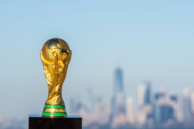 Der goldene FIFA WM-Pokal leuchtet vor der Skyline einer Metropole – ein ikonisches Bild der Fußball-Weltmeisterschaft 2026, die in den USA, Kanada und Mexiko ausgetragen wird. Der Pokal ist das begehrteste Objekt im Weltfußball. (Copyright Depositphotos.com)