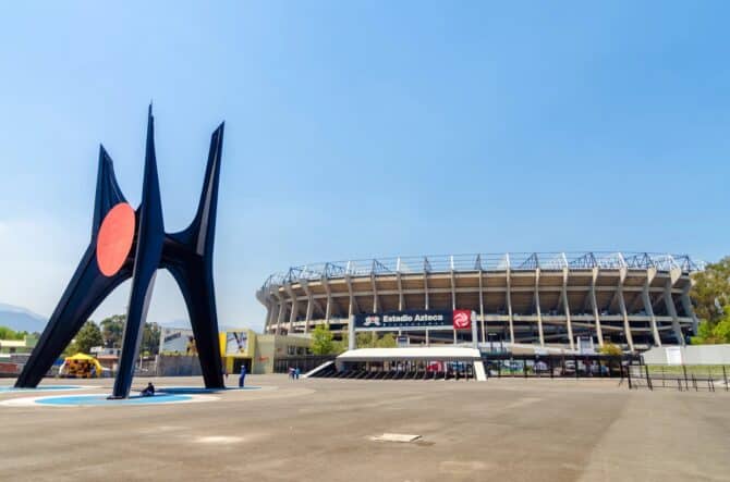 Das Aztekenstadion (Estadio Azteca) in Mexiko-Stadt mit der markanten Calder-Skulptur „El Sol Rojo“ im Vordergrund. Die Arena ist Schauplatz des Eröffnungsspiels der Weltmeisterschaft 2026. (Copyright Depositphotos.com)