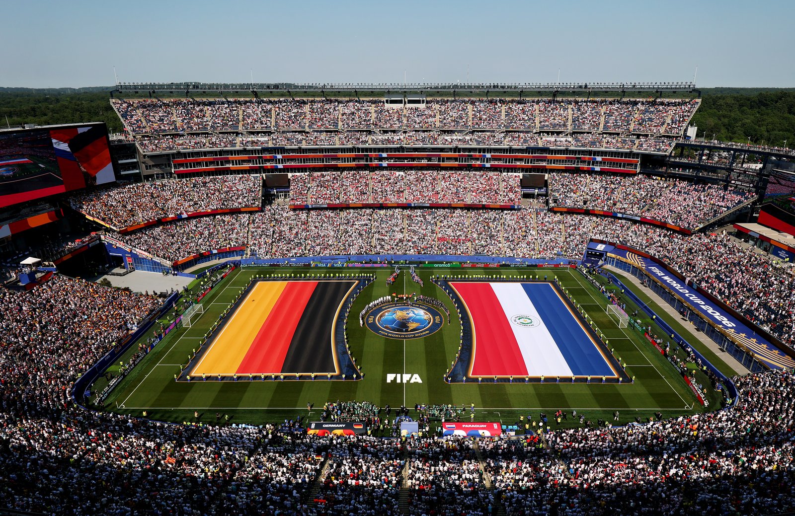 Riesige Nationalflaggen von Deutschland und Paraguay bedecken den Rasen, während sich beide Mannschaften und das Schiedsrichtergespann vor dem Anpfiff im prall gefüllten Boston Stadium aufstellen. Aufgenommen vor dem Sechzehntelfinale der WM 2026 zwischen Deutschland und Paraguay in Foxborough am 29. Juni 2026. (Darrian Traynor / Getty Images)