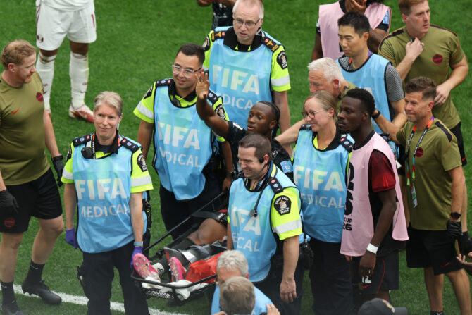 Ismaël Koné winkt auf einer Trage liegend den Zuschauern zu, umringt von Sanitätern in blauen FIFA-Medical-Westen.