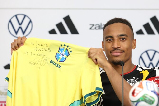 Jamie Leweling hält bei einer Pressekonferenz der deutschen Nationalmannschaft an der Winston-Salem State University ein Trikot der brasilianischen Nationalmannschaft mit einer persönlichen Widmung der Fußball-Legende Ronaldo in den Händen. Der Termin fand am 23. Juni 2026 in Winston-Salem, North Carolina, statt. (Alexander Hassenstein / Getty Images)