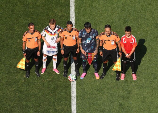 Die Kapitäne Joshua Kimmich (Nummer 6, Deutschland) und Gustavo Gomez (Nummer 15, Paraguay) posieren beim Wimpeltausch gemeinsam mit dem Schiedsrichtergespann und einem Einlaufkind für die Fotografen. Aufgenommen vor dem Sechzehntelfinale der WM 2026 zwischen Deutschland und Paraguay im Boston Stadium in Foxborough am 29. Juni 2026. (Darrian Traynor / Getty Images)