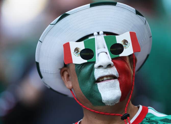 Mexikanischer Fan mit Sombrero und grün-weiß-rot bemaltem Gesicht auf der Tribüne