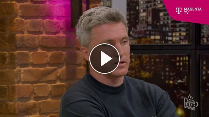 MagentaTV-Experte Micky Beisenherz im pinken Shirt im Breakfast-Club-Studio, während die Runde über die deutsche Offensivform und den Vergleich mit England und Thomas Tuchel spricht.