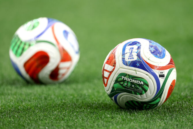 Zwei offizielle WM-Spielbälle des Modells Trionda Pro liegen auf dem Rasen des Stadions.