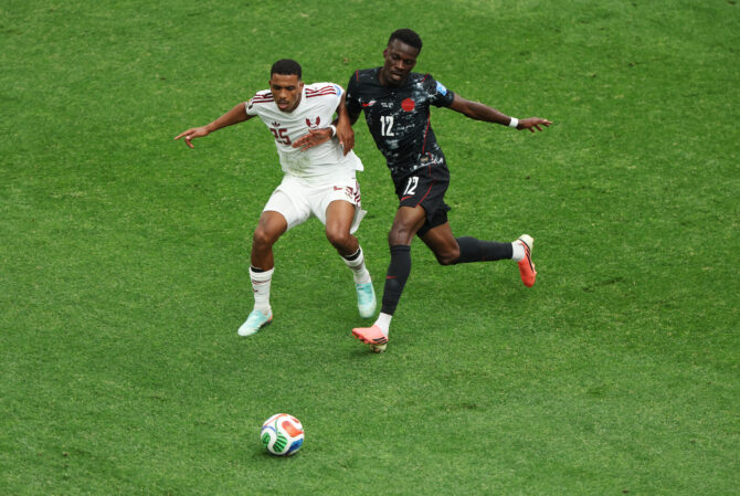 Ein kanadischer und ein katarischer Spieler laufen im Zweikampf dem Ball hinterher.