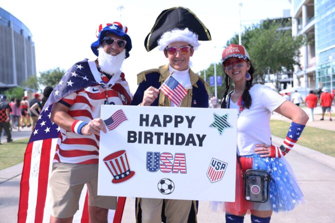 Kostümierte US-Fans feiern vor dem WM-2026-Achtelfinale zwischen Kanada und Marokko mit einem Schild den amerikanischen Unabhängigkeitstag am 4. Juli. Die Aufnahme entstand vor dem Houston Stadium in Houston, Texas. Lars Baron / Getty Images North America via Getty Images